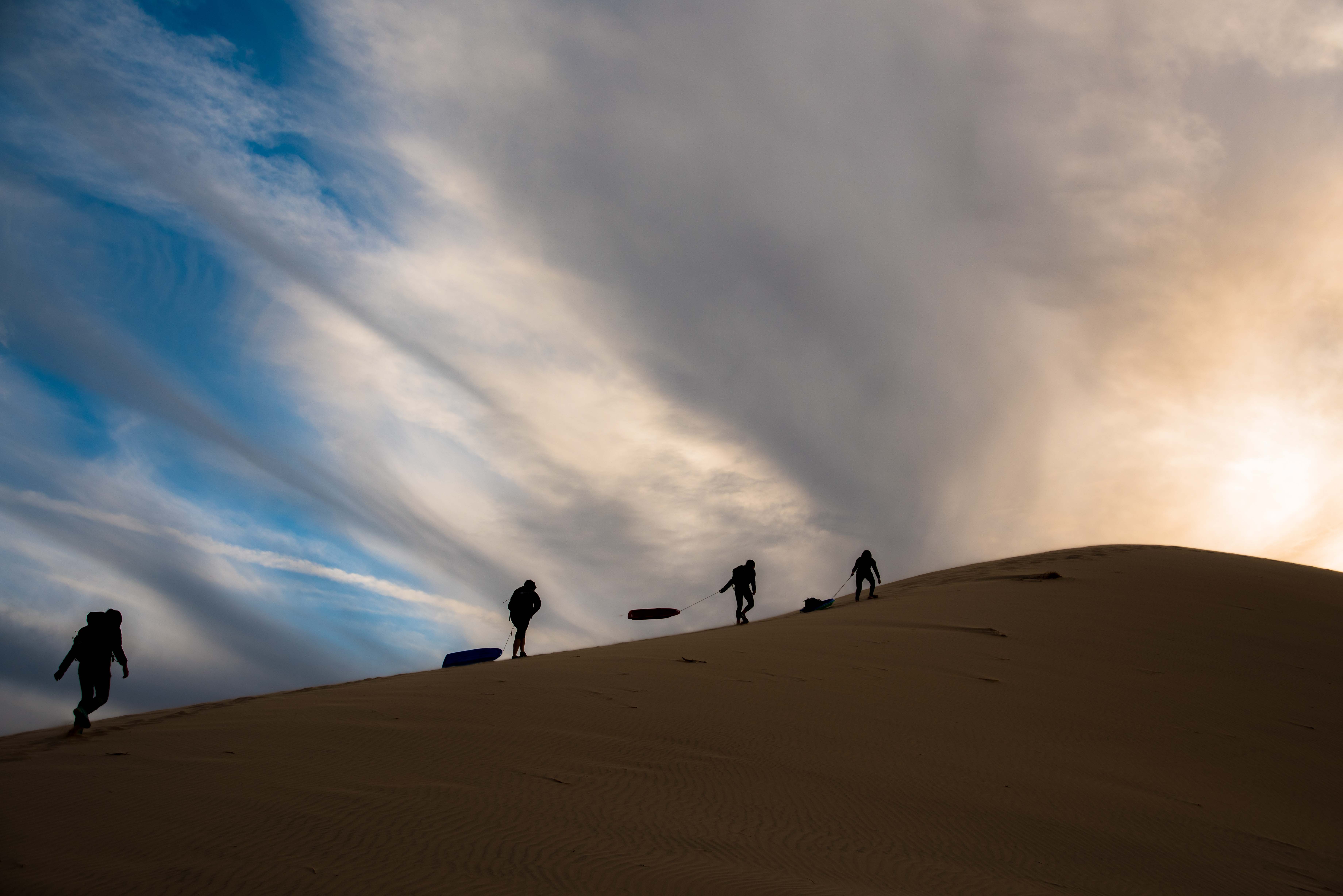 Visitors carrying sandboards to the summit of Kelso Dunes 